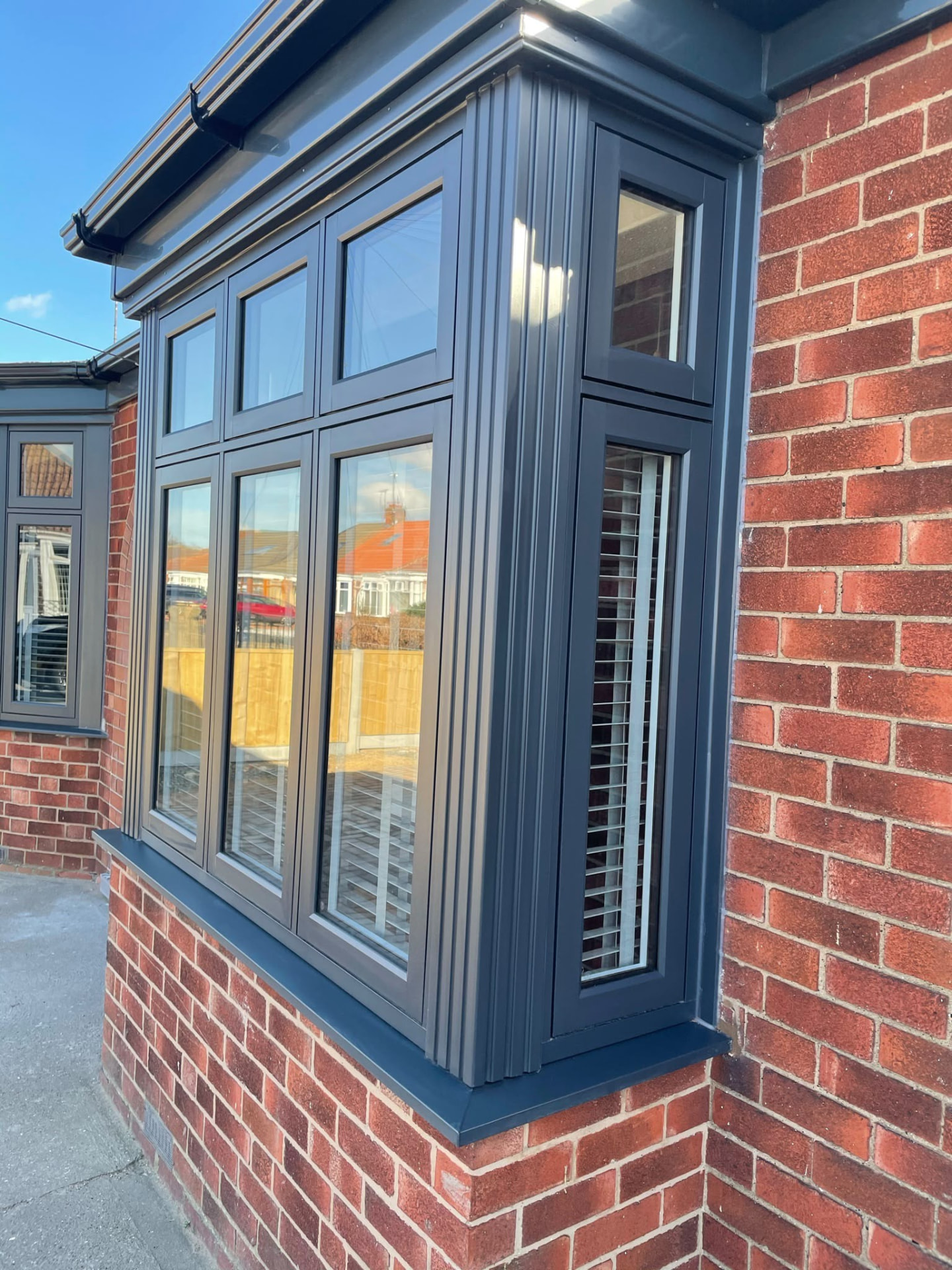 Anthracite grey bay window with shutters fitted to a red brick home