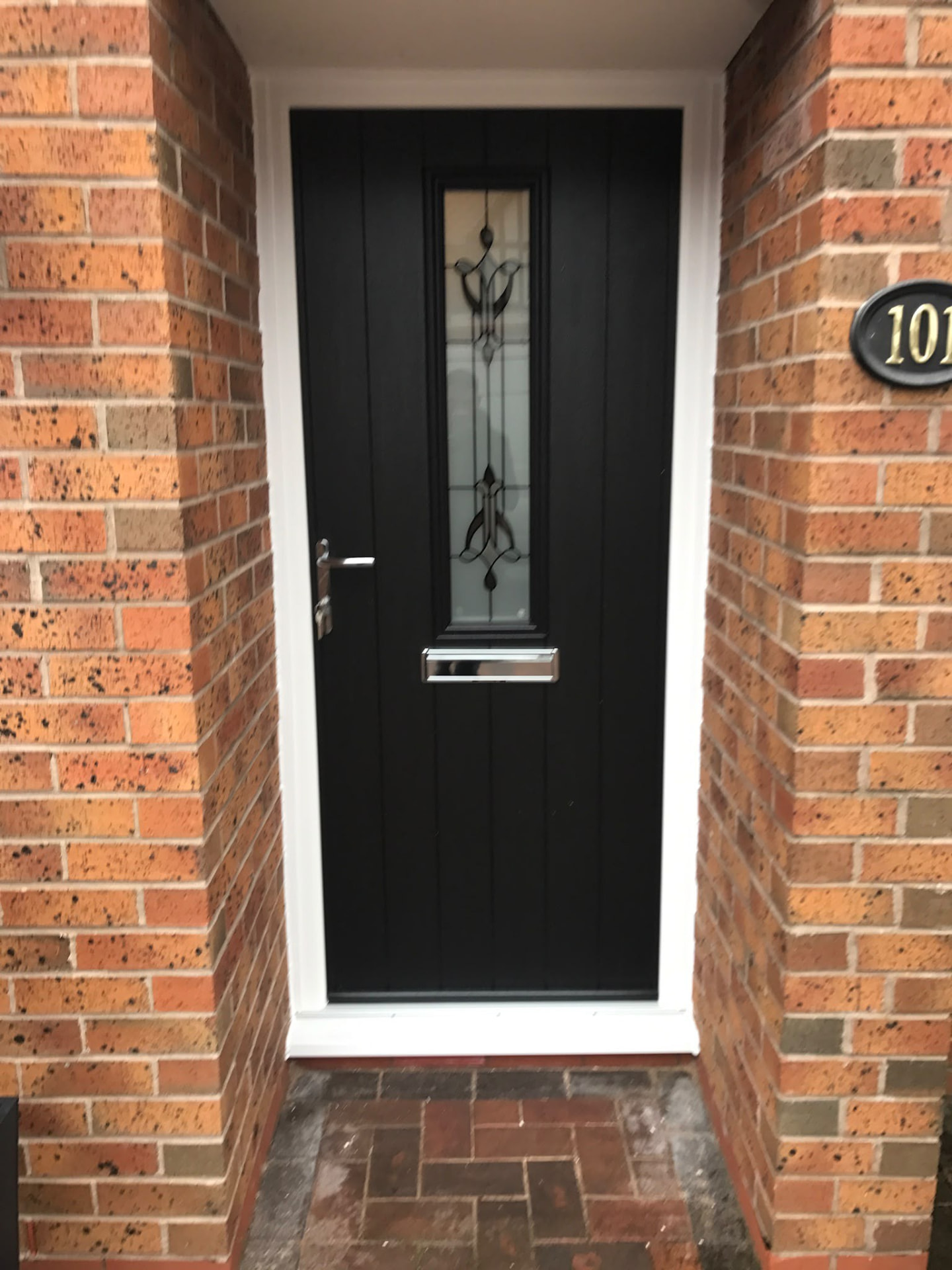 Black composite front door with decorative glass in a red brick opening
