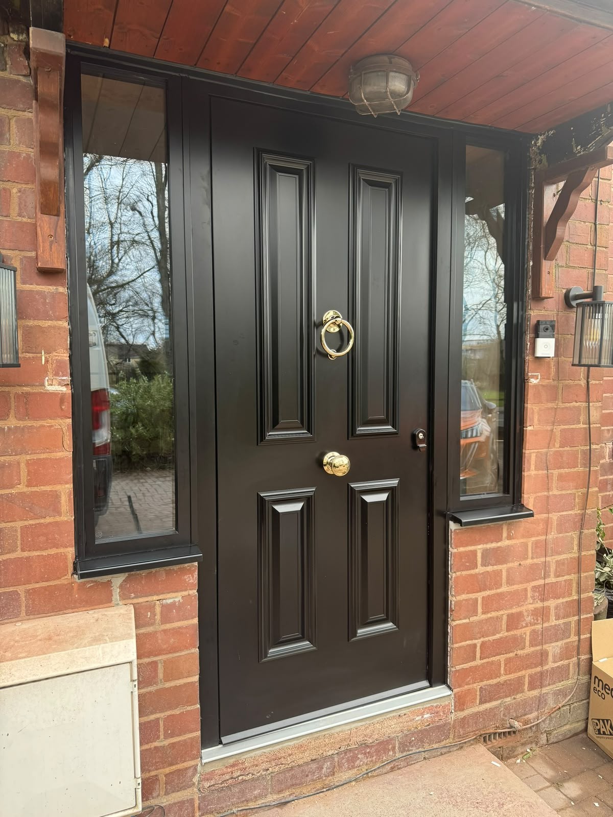 Black composite front door with brass furniture under a brick porch