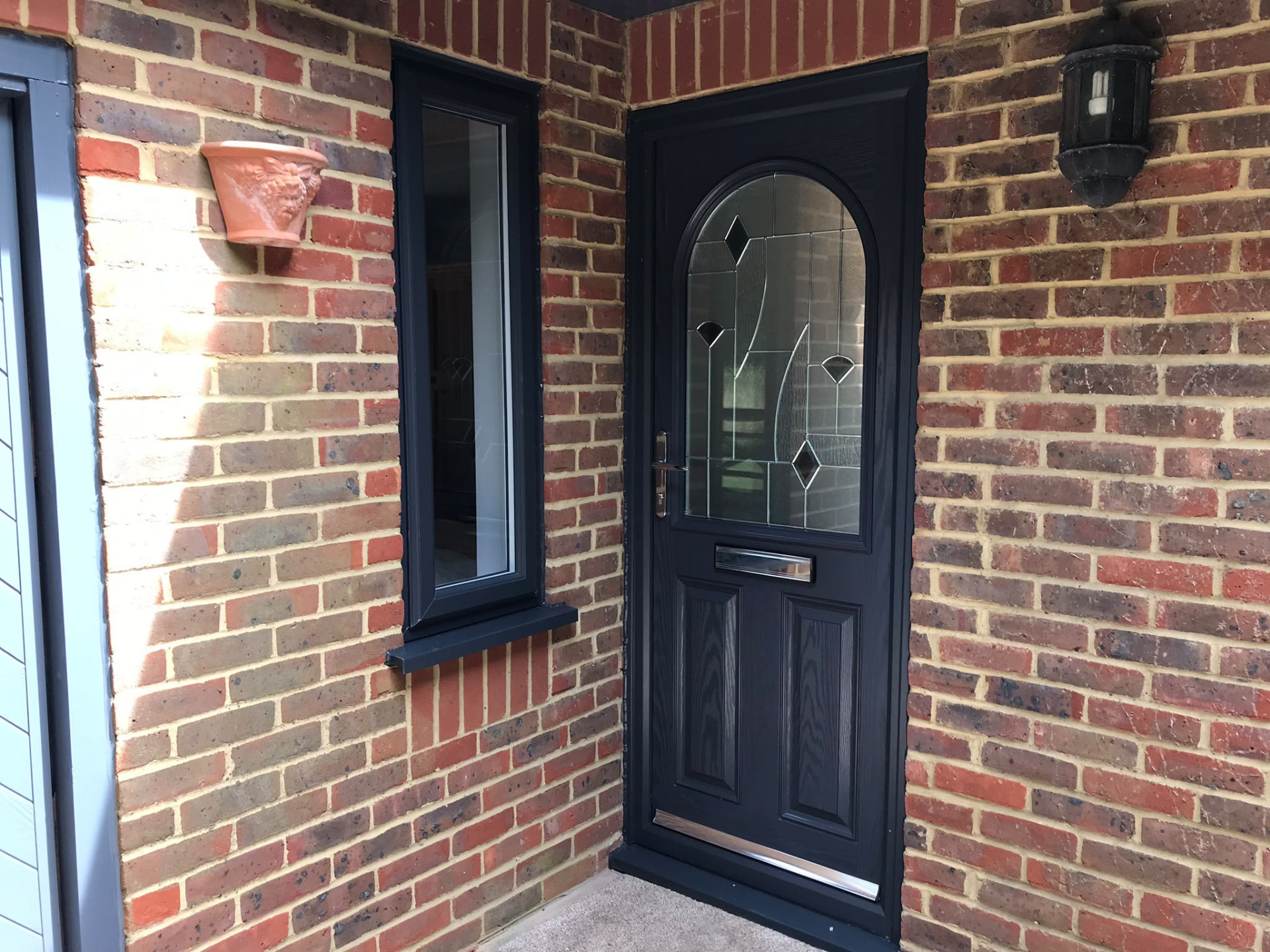 Black composite front door with arched glazing on a red brick home